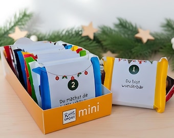 May include: An orange box of mini chocolate bars with white wrappers. The wrappers have numbers and text in German, with festive Christmas decorations. The box is labeled "Ritter Sport mini".