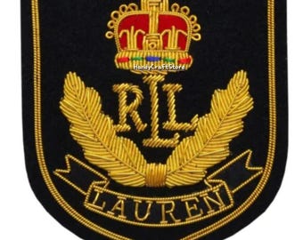 May include: Black embroidered patch with gold and red accents. Features a crown, the letters "RL", and the word "LAUREN" in gold thread. The patch has a shield shape and a gold border.
