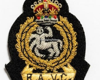 May include: A black embroidered patch featuring a gold crown with red accents, a silver horse, and a gold wreath. The patch has the letters "R.A.V.C." in gold. The patch is likely a military or organizational emblem.