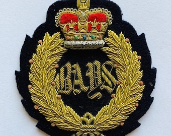 May include: A black embroidered patch featuring a gold laurel wreath and a crown with red and gold accents. The patch has the letters "BAIS" in gold. The patch is likely for a uniform or decorative item.