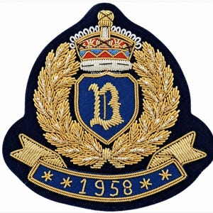 May include: A navy blue embroidered patch featuring a central shield with a gold letter B, surrounded by gold wheat stalks and topped with a crown in red, white, and blue. A blue banner at the bottom displays the gold text 1958 with star accents.