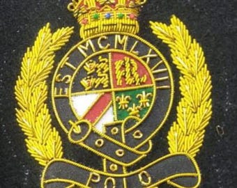 May include: Embroidered patch featuring a gold crown, laurel leaves, and a central emblem with the text "ST MCM LVII POLO." The emblem has a shield design with red, white, green, and gold elements, all on a black background.