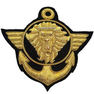 May include: A black and gold embroidered patch featuring a lion's head within a circular frame, an anchor, and wings. The text "HandyCraftStore" is visible. The patch is likely for a jacket or uniform, with a nautical or military theme.
