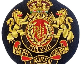 May include: Embroidered navy blue patch featuring a gold crown, two gold lions, and the text "ESTABLISHED" and "RALPH LAUREN". The center has a red emblem with the letters "RL" and the Roman numeral "MCLXVII".