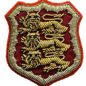 May include: A shield-shaped patch with a red background and gold embroidery. Three gold lions are embroidered on the shield. The border is red and gold. The text "HandyCraftStore" is visible.