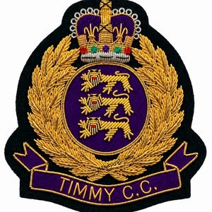 May include: A black embroidered patch featuring a gold crown with colorful accents above a purple circular emblem containing three gold lions. A gold laurel wreath surrounds the emblem, and a purple banner at the bottom reads TIMMY C.C.