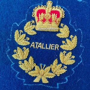 Peut inclure: Écusson brodé bleu avec une couronne dorée et des détails rouges au-dessus d'une couronne de laurier dorée. Le mot "ATALLIER" est brodé en or à l'intérieur de la couronne. L'écusson a un bord festonné.