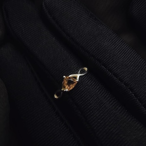 Könnte beinhalten: Ein silberner Ring mit einem birnenförmigen, hellbraunen Edelstein. Der Ring hat ein zartes, offenes Design mit poliertem Finish. Der Edelstein ist in einer Krappenfassung gefasst und der Ring wird vor dunklem Hintergrund präsentiert.
