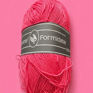 Könnte beinhalten: Ein Knäuel leuchtend rosa Garn mit einem schwarz-weißen Etikett mit der Aufschrift "Formidable". Das Garn ist fest gewickelt, und das Etikett zeigt ein Logo. Der Hintergrund ist einfarbig rosa und erzeugt einen auffälligen Kontrast. Dieses Garn ist perfekt für Strick- und Häkelprojekte.