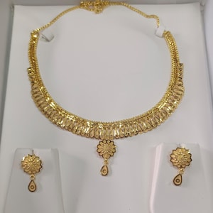 Pode incluir: Um conjunto de joias douradas com um colar e brincos a condizer. O colar apresenta um design floral com um pendente central. Os brincos tamb&eacute;m t&ecirc;m um design floral com um pendente em forma de gota. O conjunto &eacute; exibido numa superf&iacute;cie branca.
