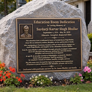 May include: A large, rough-hewn gray granite boulder features a rectangular bronze plaque titled Education Room Dedication in memory of Sardarji Kartar Singh Bhullar, including his portrait, dates, and a biographical inscription in English.