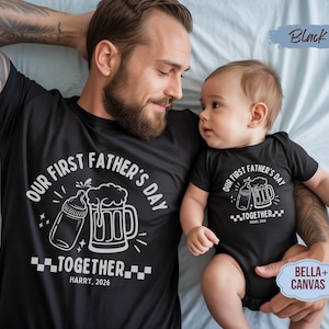 May include: Black matching t-shirts and onesie set. The shirts feature a white graphic with the text "OUR FIRST FATHER'S DAY TOGETHER" and a baby bottle and beer mug design. The year "2026" is also included.