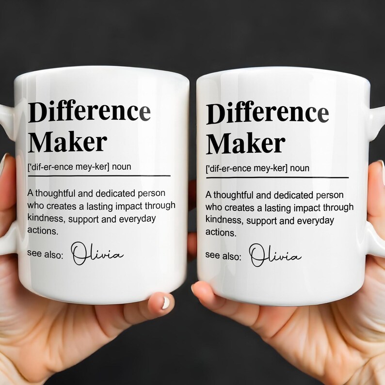 May include: Two white ceramic mugs featuring black printed text that defines the term Difference Maker as a thoughtful and dedicated person who creates a lasting impact through kindness, support and everyday actions, with the name Olivia listed below.