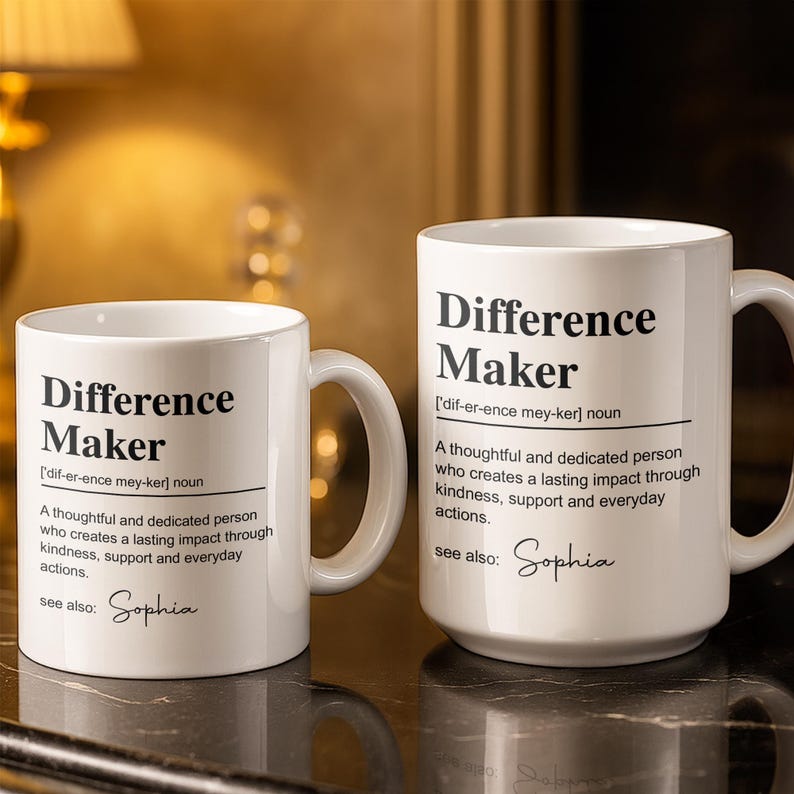 May include: Two white ceramic mugs featuring black printed text that defines the term Difference Maker as a thoughtful and dedicated person who creates a lasting impact through kindness, support and everyday actions, with the name Sophia listed below.