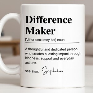 May include: A white ceramic mug featuring black printed text that defines the term Difference Maker as a thoughtful and dedicated person who creates a lasting impact through kindness, support and everyday actions, with the name Sophia listed below.