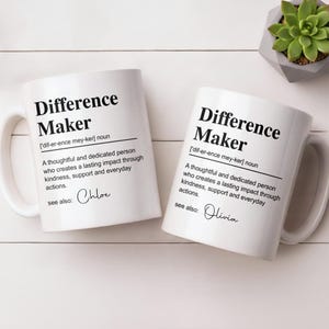 May include: Two white ceramic mugs featuring black text that defines the term Difference Maker as a thoughtful and dedicated person who creates a lasting impact through kindness, support and everyday actions, with the names Chloe and Olivia printed.