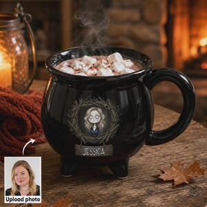 May include: A black cauldron-shaped ceramic mug filled with hot cocoa and marshmallows, featuring a stylized illustration of a person with blonde hair inside a twig wreath and the name JESSICA printed on a wooden sign graphic below the image.