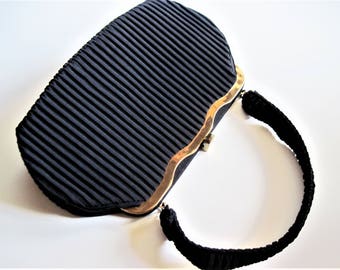 May include: A black pleated evening bag with a gold clasp and a black fabric handle.