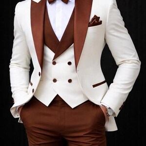 May include: A formal ivory suit with brown accents. The suit includes a jacket with brown lapels, a matching vest, and trousers. A brown bow tie and pocket square complete the ensemble. The image has the text "FASHION BLOOM STUDIO".