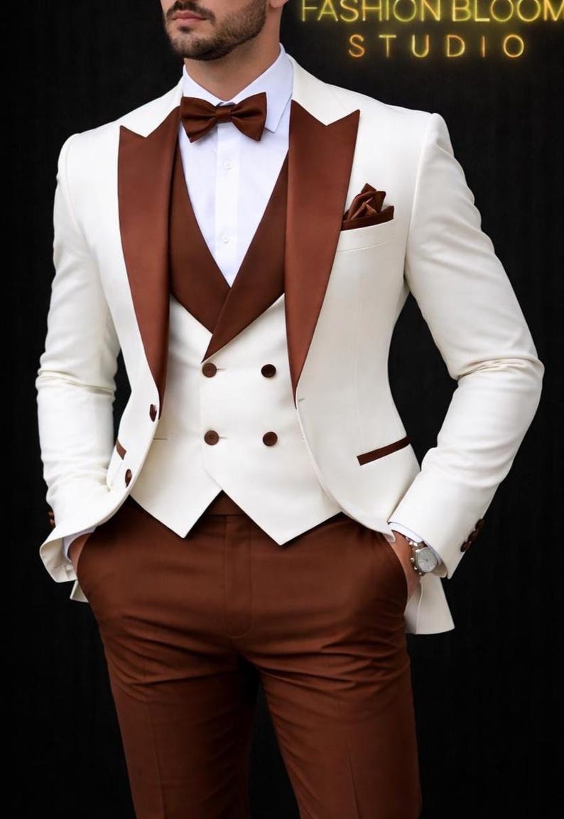 May include: A formal ivory suit with brown accents. The suit includes a jacket with brown lapels, a matching vest, and trousers. A brown bow tie and pocket square complete the ensemble. The image has the text "FASHION BLOOM STUDIO".