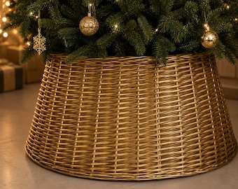 May include: A gold-colored woven wicker Christmas tree collar with a tapered, conical shape. The base is wide and circular, featuring a tight, horizontal weave pattern that conceals the bottom of a green pine tree decorated with gold ornaments.