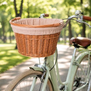 Może przedstawiać: Jasnobrązowy wiklinowy kosz rowerowy z beżową podszewką z tkaniny jest zamontowany na kierownicy miętowego roweru. Kosz jest okrągły i ma pleciony wzór. Rower ma brązowe skórzane akcenty.