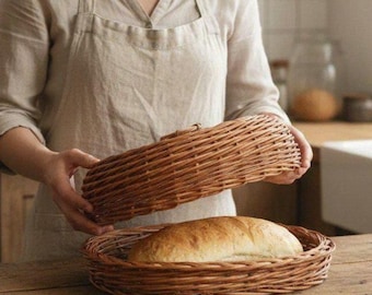 May include: A round, woven wicker bread basket with a matching lid. The basket is made of natural brown willow reeds and features a shallow, circular base containing a single loaf of golden-brown, crusty artisan bread.