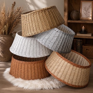 Puede incluir: Una pila de cinco collares para árbol redondos de mimbre trenzado en varios colores, incluyendo bronceado natural, gris plateado, blanco, marrón oscuro y un beige claro con borde marrón oscuro. Cada collar tiene una forma cilíndrica cónica.