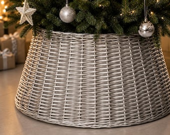 May include: A silver-colored woven wicker Christmas tree collar with a tapered, conical shape. The collar features a tight, horizontal weave pattern and a smooth, metallic finish, designed to encircle the base of a tree and conceal the stand.