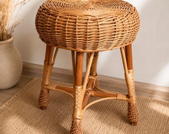 May include: A round stool featuring a woven light brown rattan seat and four sturdy wooden legs. The legs are connected by a central support structure and feature intricate woven rattan detailing at the base of each leg, providing stability.