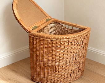 May include: A semi-circular wicker storage basket with a hinged lid. The basket features a woven light brown rattan construction with a flat back designed to sit flush against a wall. The lid is attached with metal hinges and opens upward.