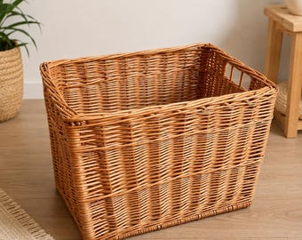 May include: A rectangular storage basket crafted from light brown woven wicker. The basket features a sturdy, open-top design with integrated side handles built into the rim, showcasing a consistent, tight weave pattern throughout the structure.