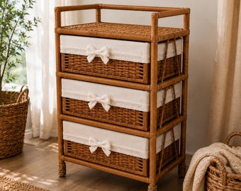 May include: A three-tier storage unit crafted from brown woven rattan, featuring a flat top surface and three rectangular drawers. Each drawer is lined with a cream-colored fabric cover, accented with a delicate lace trim and a small fabric bow.
