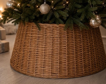May include: A round, tapered Christmas tree collar constructed from woven brown wicker. The collar features a tight, horizontal weave pattern and sits at the base of a green pine tree decorated with silver ornaments and warm white string lights.