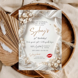 May include: An invitation for Sydney's 30th birthday, featuring elegant pearl and satin accents. The invitation includes the date, time, and location, with a red lipstick graphic. The design is set on a wooden tray with decorative elements.