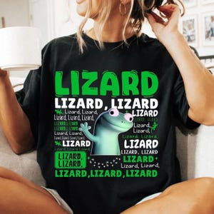 May include: Black t-shirt with the word "LIZARD" in large green letters. The shirt features a cartoon lizard with a friendly expression and the word "Lizard" repeated in various sizes and fonts.