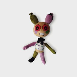 May include: A plush toy bunny with a tan face, red eyes, and a stitched mouth. The bunny has green, purple, and pink limbs, a white shirt with purple and green polka dots, and a black bow tie. The ears are green and purple.