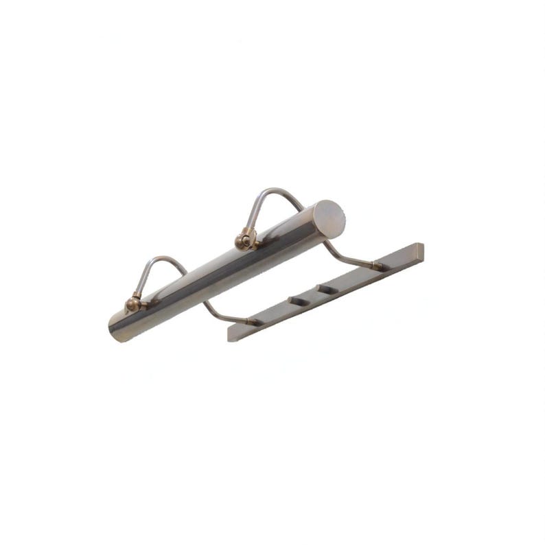 May include: A silver-toned picture light with a cylindrical body and curved arms. The light has a rectangular base with three slots. The fixture is designed to illuminate artwork or photographs.