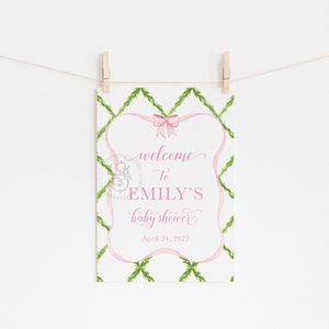 May include: A pink and green baby shower welcome sign with a pink ribbon and bow. The sign reads "Welcome to Emily's Baby Shower April 24, 2022".