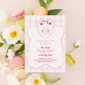 May include: Pink and white gingham patterned invitation with a cherry and bow on top. The invitation reads "She's our cherry on top & so much fun. Our Sweet Emily Kate is turning One! Saturday, June 10 - 2:00 pm. The Sullivan Home, 55 Main Street, Baltimore. RSVP to Amber - 410.555.3535"