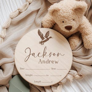 May include: A round wooden plaque with a duck silhouette and the text "Jackson Andrew" engraved on it. The plaque has spaces to record the date, time, weight in pounds and ounces, and length in inches.