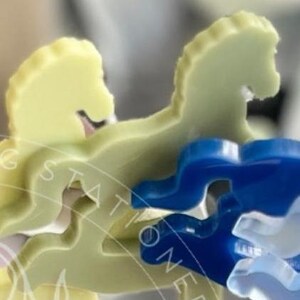 May include: A set of flat, horse-shaped acrylic pieces in pale yellow and translucent blue. The pieces feature a smooth, die-cut silhouette of a horse in a galloping pose. A faint, circular watermark with text is overlaid across the objects.