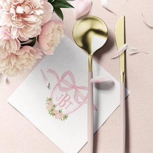 May include: A gold and light pink spoon and knife set placed next to a white square napkin featuring a pink ribbon, floral wreath, and the letters JBr. A bouquet of light pink peonies with green leaves is positioned in the upper left corner.