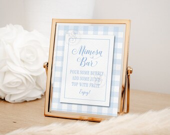 May include: A gold-framed sign with a blue and white gingham background. The sign says "Mimosa Bar" and includes instructions for making a mimosa: "Pour some bubbly, add some juice, top with fruit, Enjoy!"