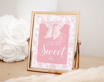 May include: A pink and white sign with a gold frame and a white bow. The sign says "Oh So Sweet" in white cursive lettering.