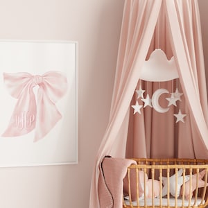 May include: A pink and white baby crib canopy with a white cloud mobile hanging above it. The mobile has a crescent moon and stars. The crib is made of wicker and has a pink blanket inside.
