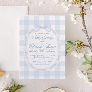 May include: A blue and white gingham baby shower invitation with a blue ribbon and a lace design. The invitation reads "Please join us for a baby shower honoring Honnie Sullivan and baby Aaron James. Saturday, September 25th, 10:30 AM. The Johnson Residence, 555 Main Street, Baltimore, MD. RSVP to Stephanie 410.555.5555. Registered at Babylist.com"