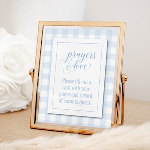May include: A gold-framed sign with a light blue gingham pattern and the words "prayers & love." The sign includes the text "Please fill out a card with your prayer and a word of encouragement."