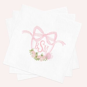May include: A stack of white square paper napkins featuring a centered watercolor illustration of a pink ribbon bow tied above a pink monogram with the letters BSM, accented by a small cluster of pink roses and green leaves at the bottom.