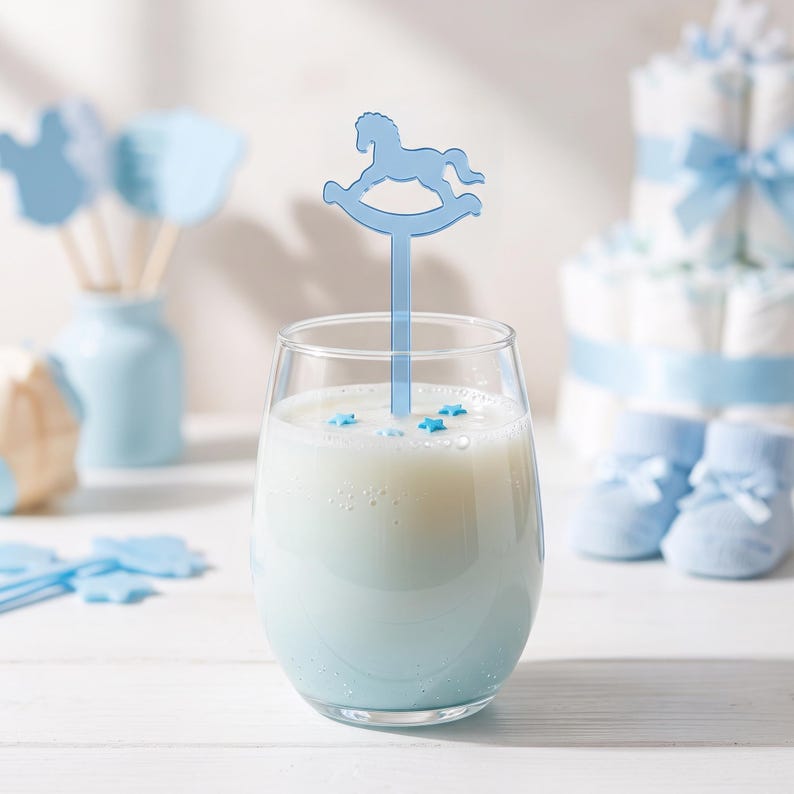 May include: A clear glass filled with a light blue liquid, featuring a light blue acrylic drink stirrer shaped like a rocking horse. The surface of the liquid is decorated with small, light blue star-shaped sprinkles, creating a festive appearance.